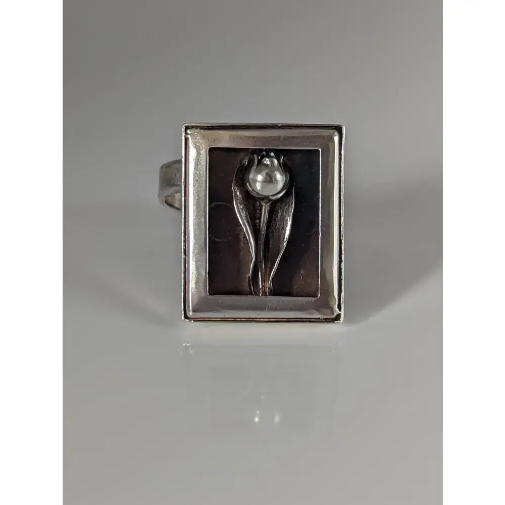 Silver steed large frame silver ring with a raised tulip design and pearl center on a dark background