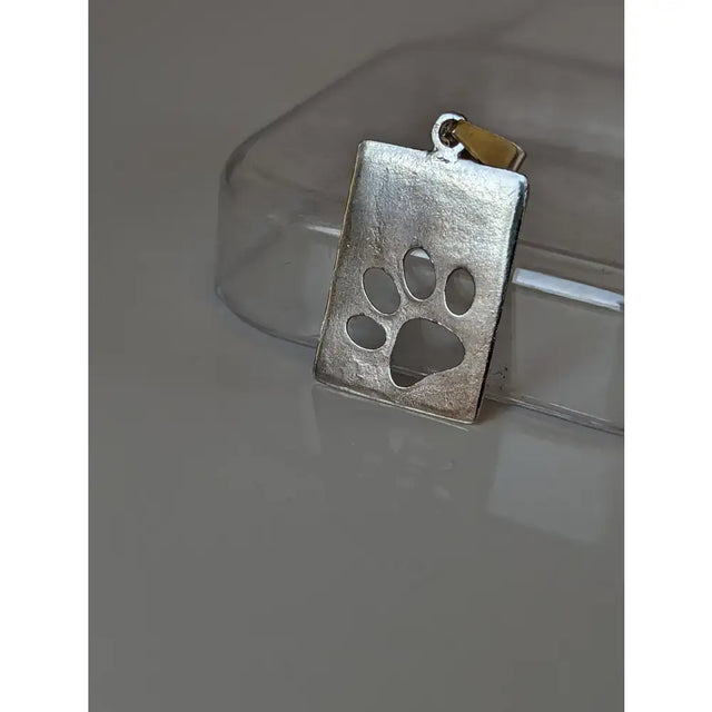 Silver pendant silver steed paw with a textured matte finish and cut out paw print tag design with gold bail