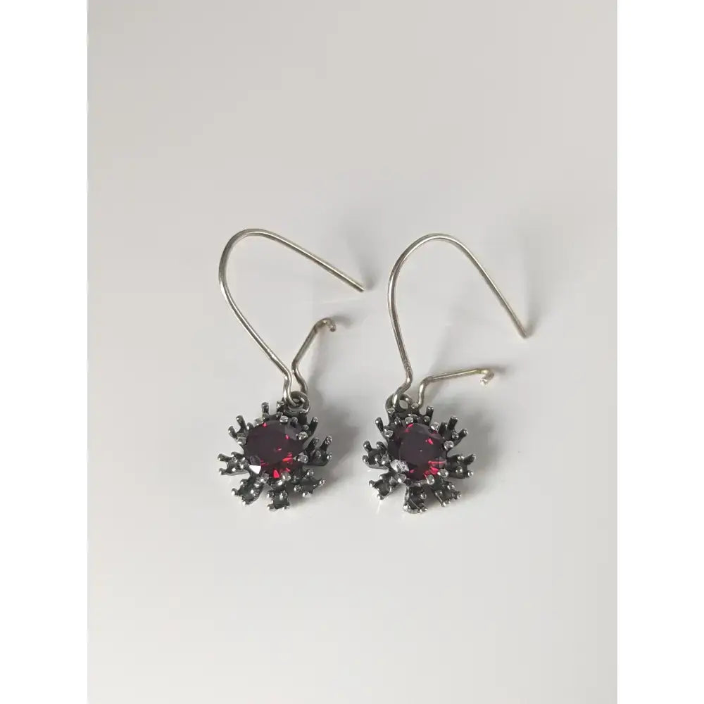 A pair of silver steed red crystal sunflower dropped earrings with dark silver hooks and deep red gemstones