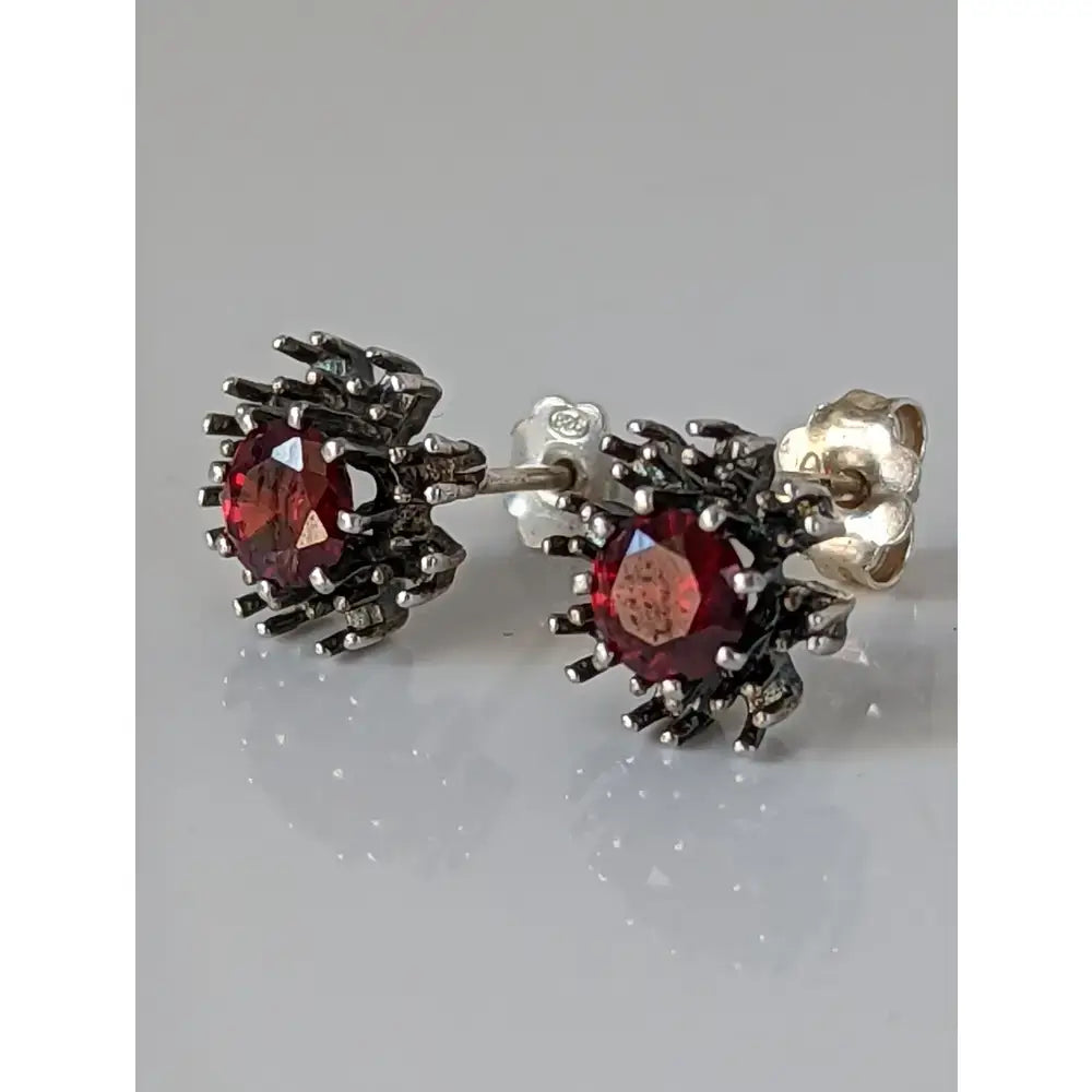 A pair of silver steed red crystal sunflower stud earrings with dark silver metal and faceted red gemstones
