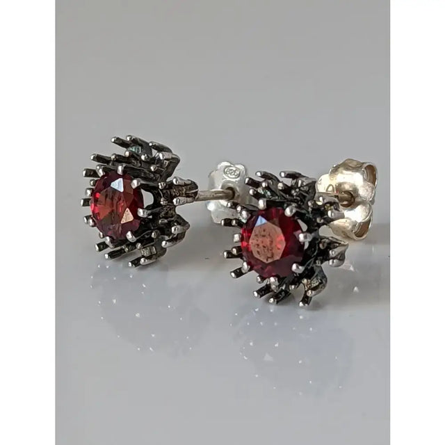 A pair of silver steed red crystal sunflower stud earrings with dark silver metal and faceted red gemstones
