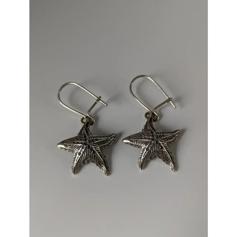 Silver steed sea star dropped earrings featuring silver star dropped earrings with textured detailing and hook clasps