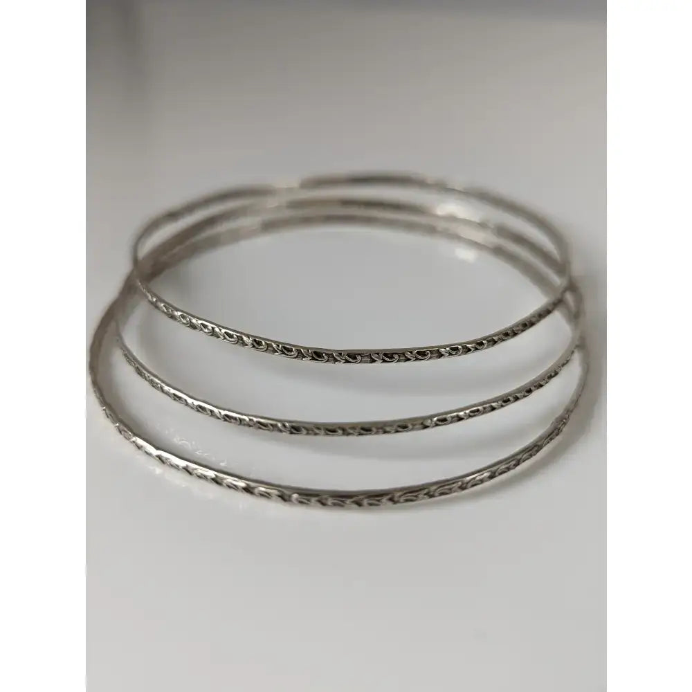 Three silver steed slim silver bangles with intricate vine patterns engraved along outer edges