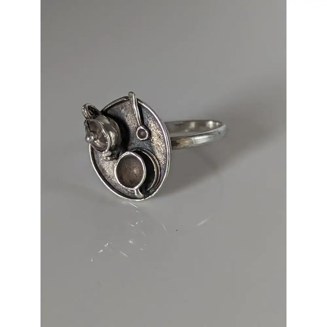 Silver steed tea silver-toned ring with circular textured face and miniature kitchenware sculptures showcasing silver craftsmanship