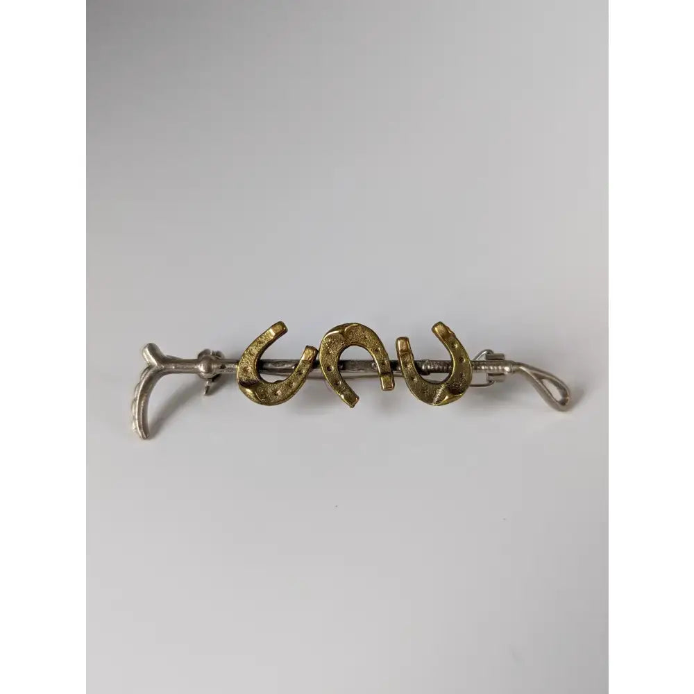 A silver steed triple cane brooch with a sleek silver hairpin and three gold accent horseshoe charms with intricate detail