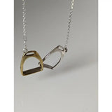 A delicate silver steed equestrian jewelry two stirrups necklace with one gold and one silver pendant on a fine chain