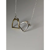 A delicate silver steed two stirrups necklace with gold and silver interlocking pendants on a fine chain