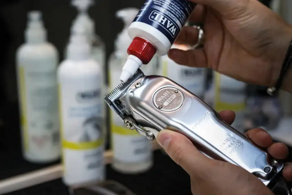 Silver wahl clipper with a red and white maintenance bottle being used to apply lubricant.