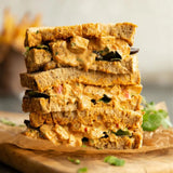Stack of golden brown whole grain simply sandwiches filled with creamy orange curry chicken and fresh greens