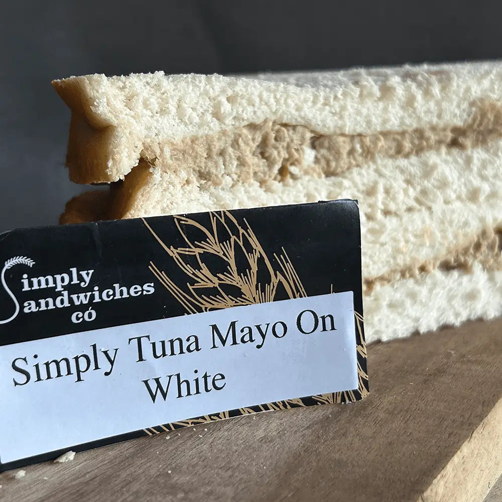 A neatly sliced tuna mayo sandwich on white bread from simply sandwiches with a branded sign for bon sweets pouches