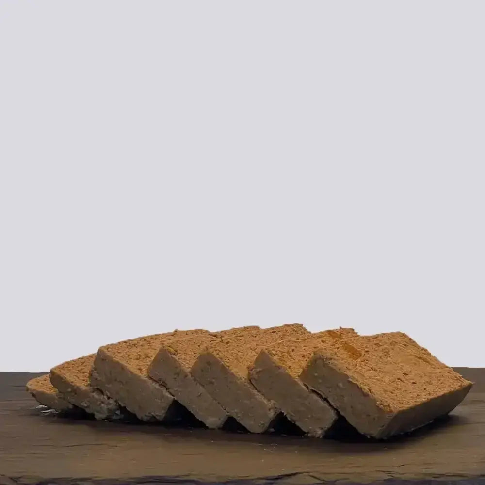 Slices of beige textured tofu arranged on dark surface for skinners field and trail adult chicken root veg wet dog food