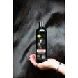 Black magic shampoo bottle with silver cap and horse label held against dark fur for smart grooming black use