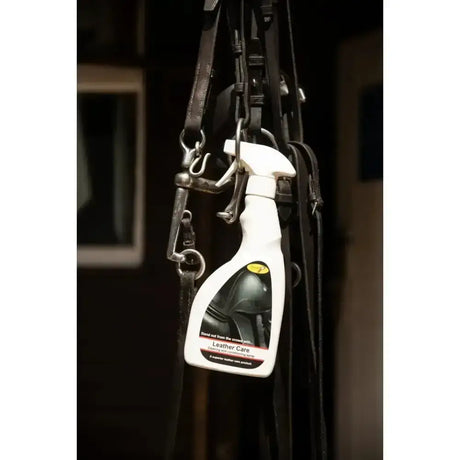 White spray bottle of smart grooming leather care spray with black and yellow label hanging among horse tack