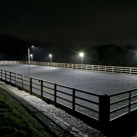 A dark gravel arena lit at night by solar technology arena 2k led lights with white railings and timed illumination mode
