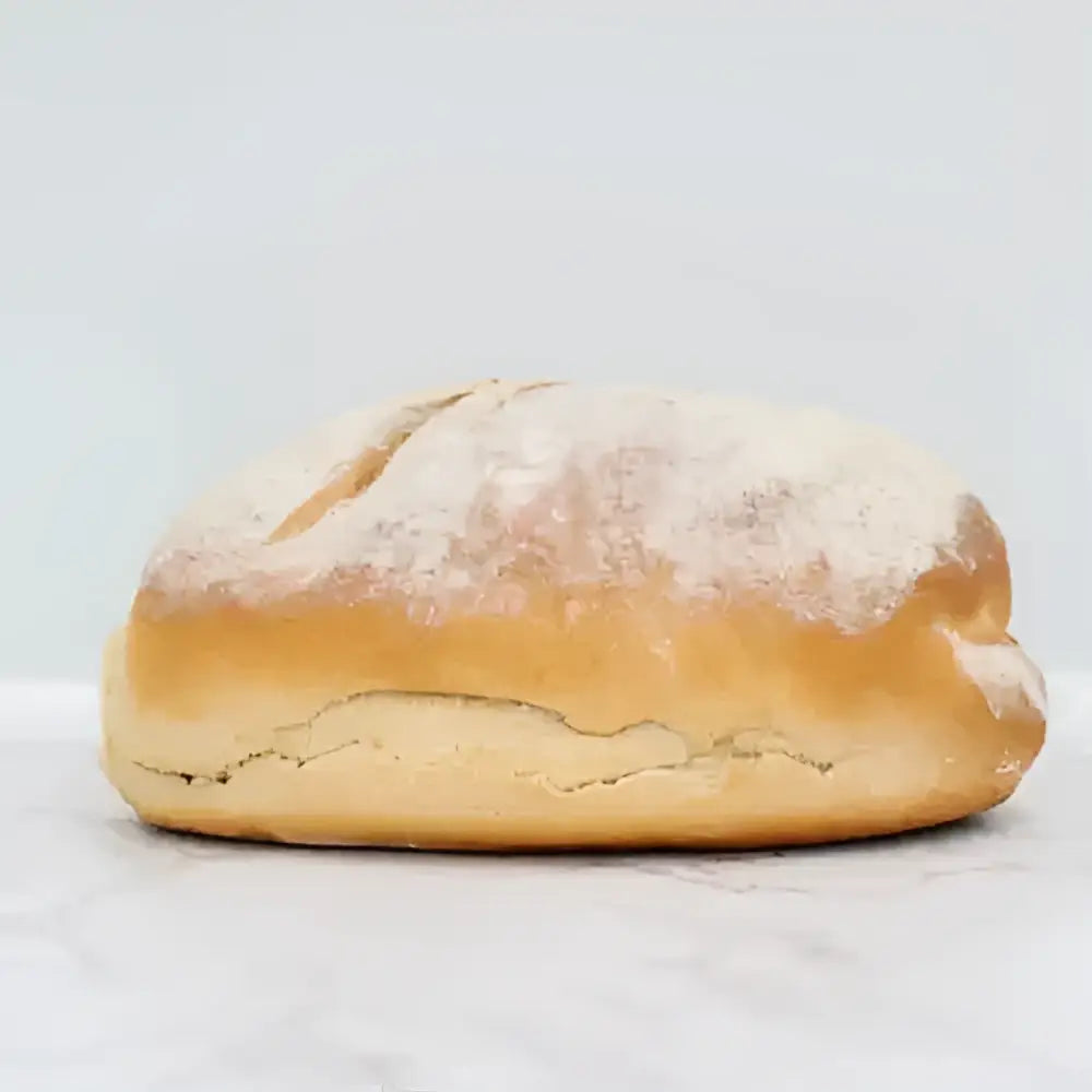 Golden-brown sourdough white bread loaf with rustic cracked crust and flour dusting on round white bread surface