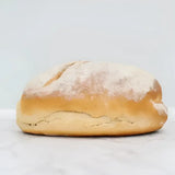 Golden-brown sourdough white bread loaf with rustic cracked crust and flour dusting on round white bread surface