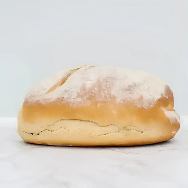 Golden-brown sourdough white bread loaf with rustic cracked crust and flour dusting on round white bread surface