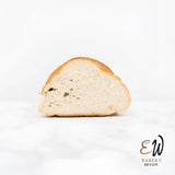 A golden-brown soft sourdough white bread loaf with a crusty exterior and airy round white interior