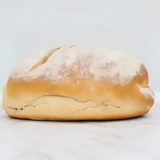 Golden-brown sourdough wholemeal bread with a rustic cracked crust and flour dusting on round white bread loaf