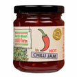 A glass jar of vibrant red hot chilli jam from south devon chilli farm with a cream label and black lid