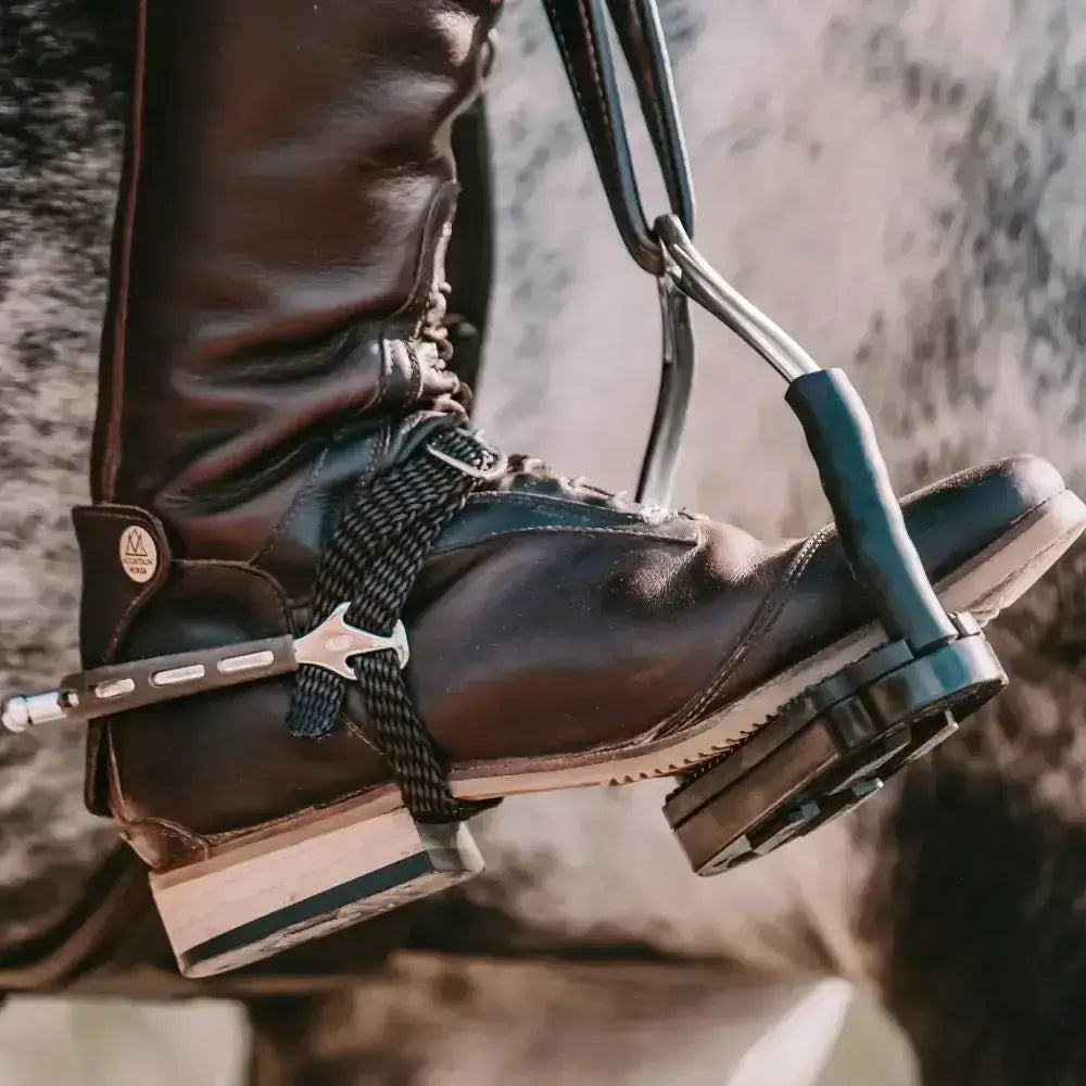 Black leather riding boot with silver spur and black strap shown with sprenger bow balance safety stirrups