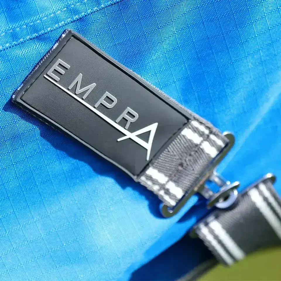 Black rectangular brand patch with silver empra logo on striped strap attached to blue stormx empra 0g turnout rug