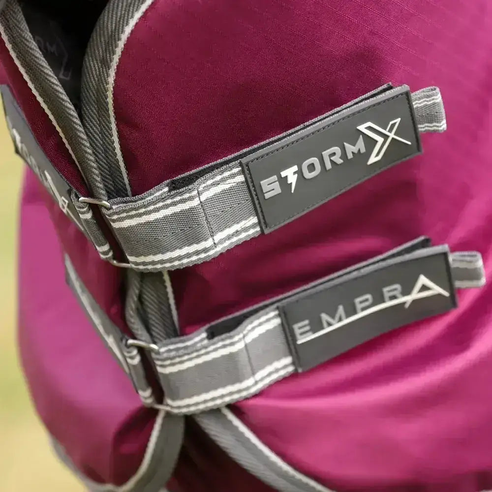 Close-up of vibrant magenta stormx empra combi turnout rug straps and branding on gray fabric with white stitching