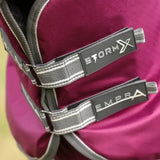 Close-up of vibrant magenta stormx empra combi turnout rug straps and branding on gray fabric with white stitching