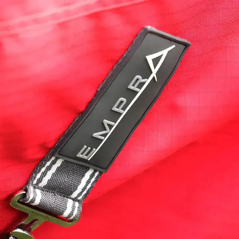 Black rectangular patch with silver empr logo and triangle on gray white strap of stormx empra combi turnout rug