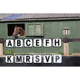 A brown horse with a white blaze peeks from a green stable window next to stubbs hook-on dressage letters markers 12