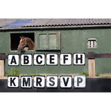 A brown horse with a white blaze looks out a green stable window beside wooden shutters in stubbs hook-on dressage letters markers 12