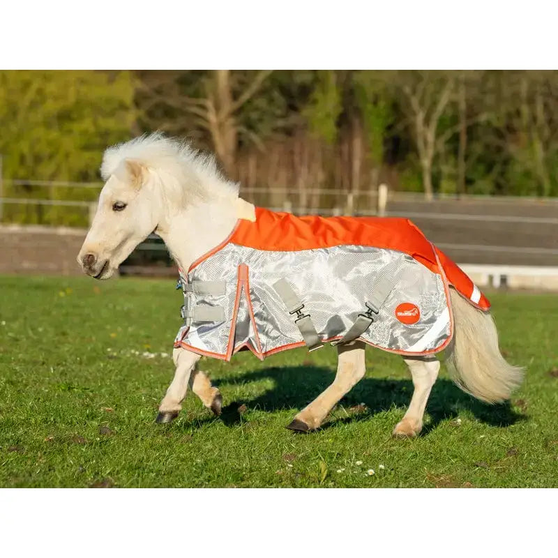 A white pony wearing a reflective silver and orange swish mini fly turnout combination rug with gray straps