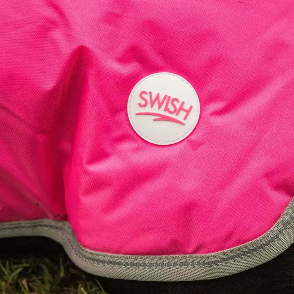 A vibrant pink swish waterproof dog coat with a white logo patch gray reinforced stitching and velcro chest closure