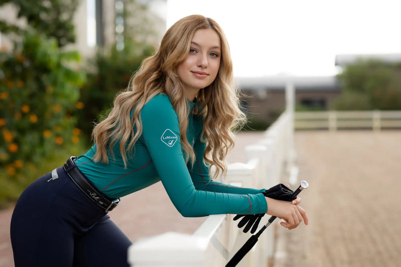 Teal long-sleeved equestrian top with a subtle logo patch on the left sleeve