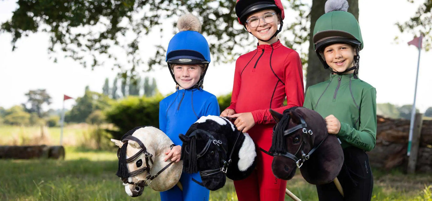 Three children in riding gear hold plush horse toys, each with distinct colors and textures.