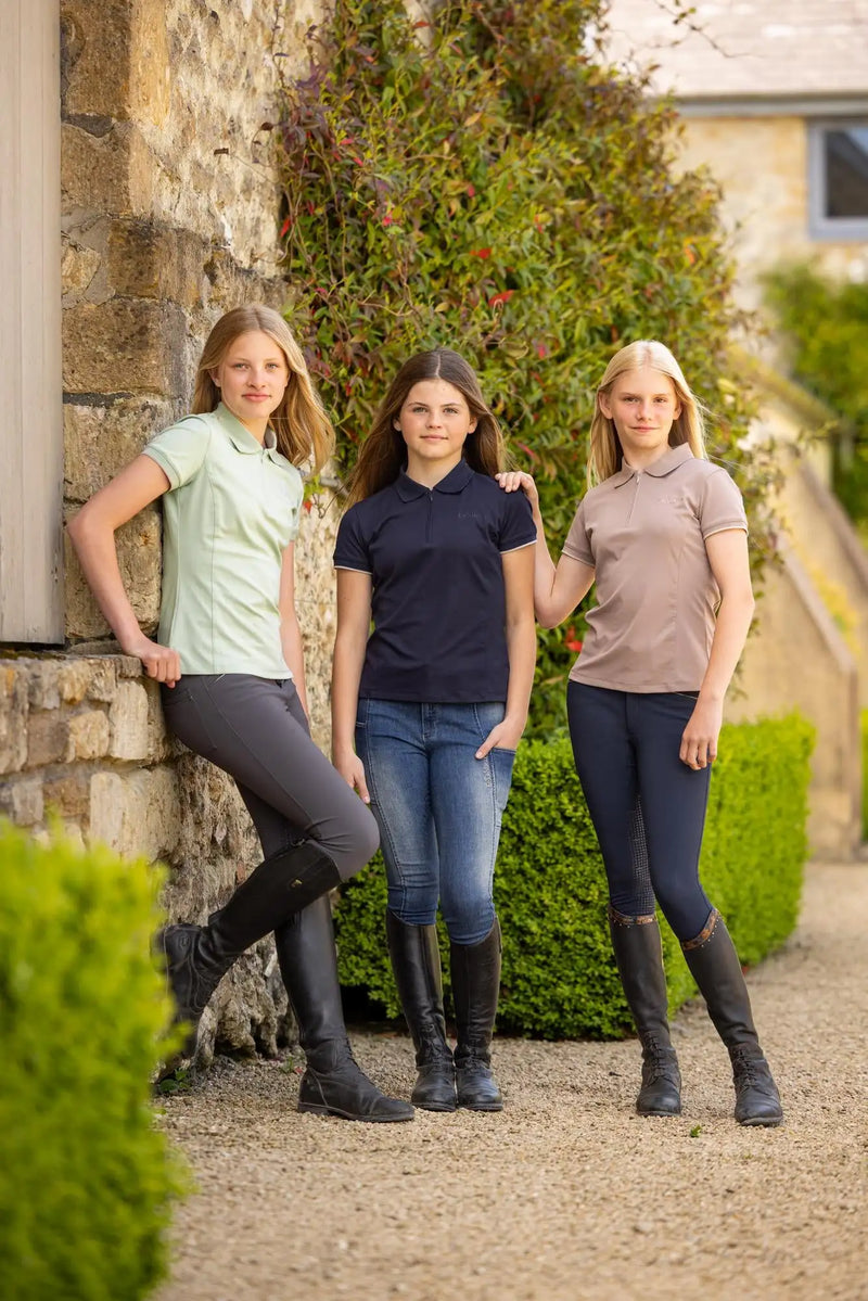 Three young women pose outdoors in matching short-sleeved polo shirts, light mint, navy blue, and taupe, with a classic collar design.