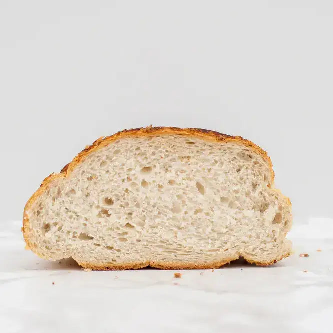 A golden brown crusty tiger bloomer round white bread with a soft airy interior and visible air pockets