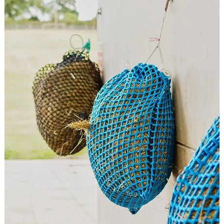 Bright blue mesh trickle net softee hay feeder hanging on wall for slow dry hay feeding in range nets style
