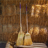 Two ultimate corn brooms with wooden handles and purple accents stand against golden hay bales for corn broom great use