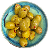 A bowl of glossy green hot honey olives 175g with red pepper flakes and garlic in a hand-painted blue dish