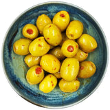 A bowl of glossy yellow west country picante pimento olives with red chili seeds and seasoning flecks