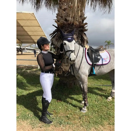 Gray horse wearing a navy blue bridle and black saddle with white protective pad next to whitaker b167 lyon performance breeches white