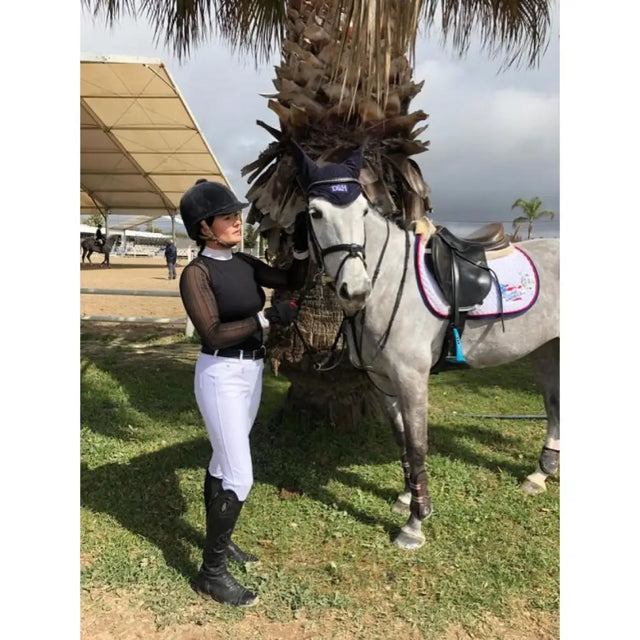 Gray horse wearing a navy blue bridle and black saddle with white protective pad next to whitaker b167 lyon performance breeches white