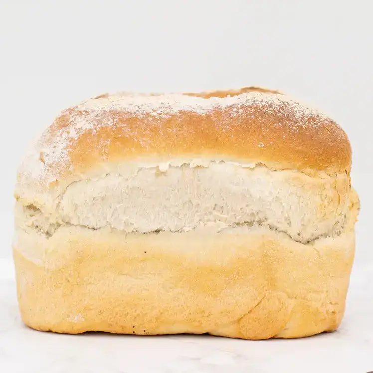 Golden brown white farmhouse loaf with soft white interior and flour dusting on a round white bread loaf
