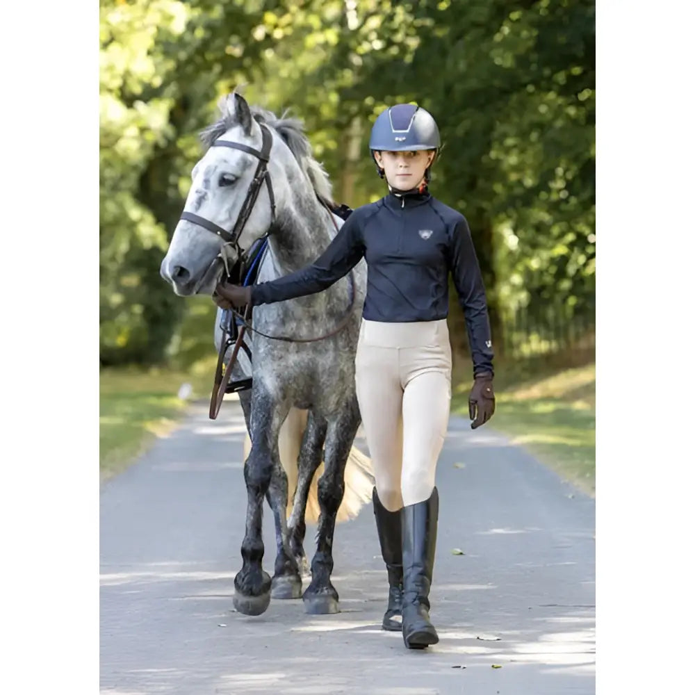 A rider in a black woof wear young rider tech shirt with iflex fabric walks beside a dapple gray horse wearing a dark helmet