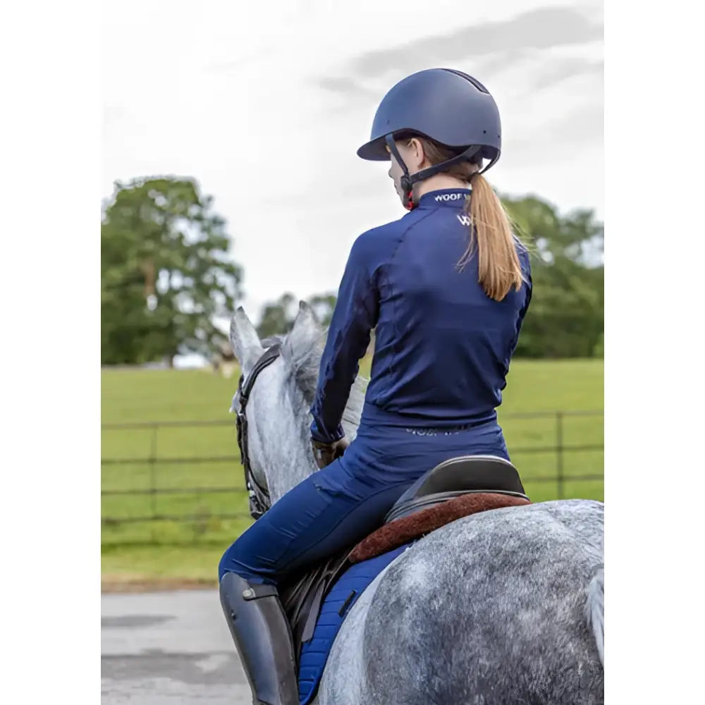 Blue riding helmet with black visor and adjustable straps paired with woof wear young rider tech shirt in iflex fabric