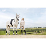 A white horse with black leg wraps stands next to a rider wearing a lemieux young rider kennedy show jacket stone