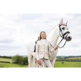 A white horse wearing lemieux black tack and a light hood stands next to a young rider kennedy show jacket stone equestrian gear